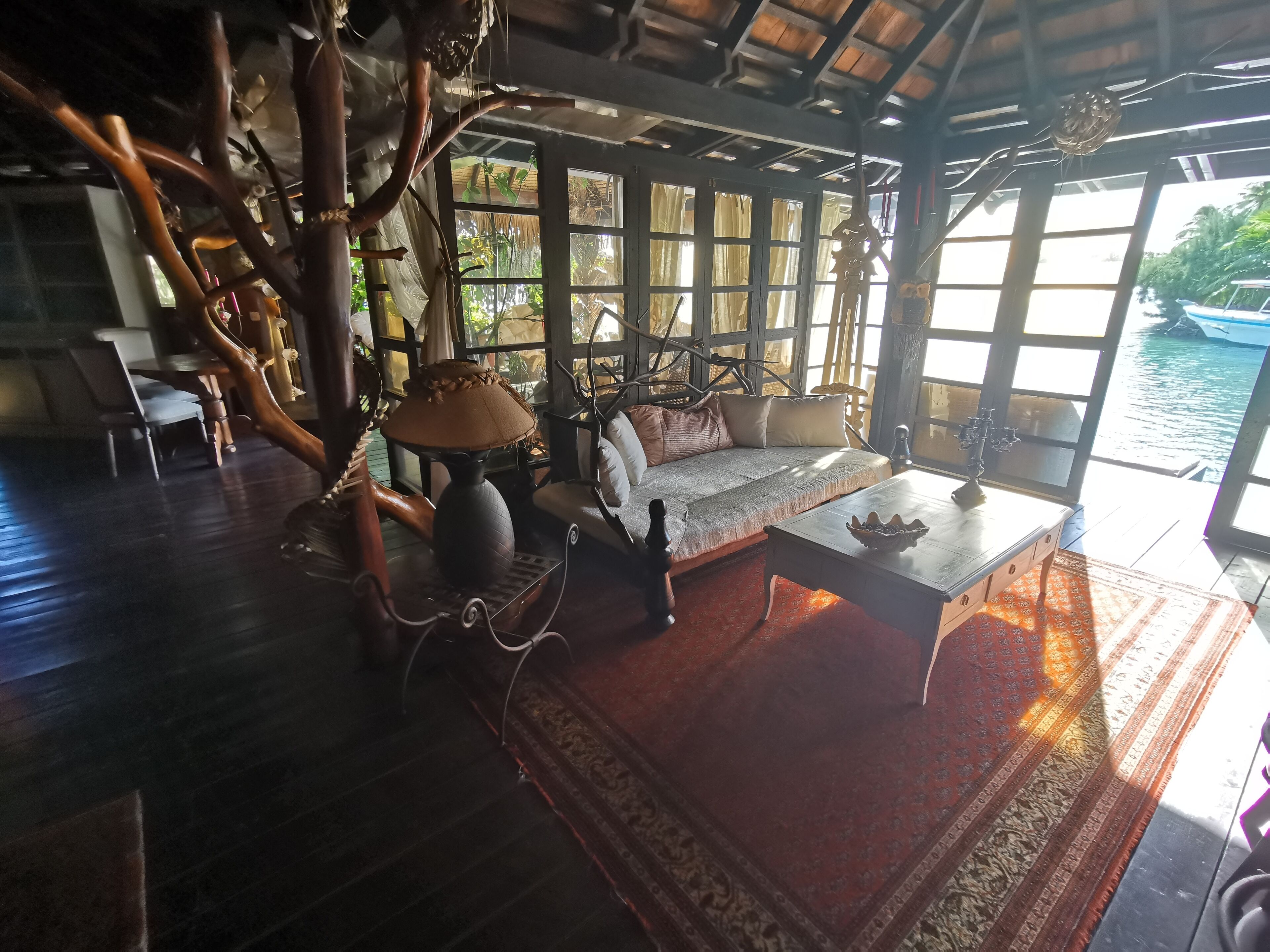 A room with a wooden floor, a sofa with cushions, a table with a bowl, and a hanging lamp.
