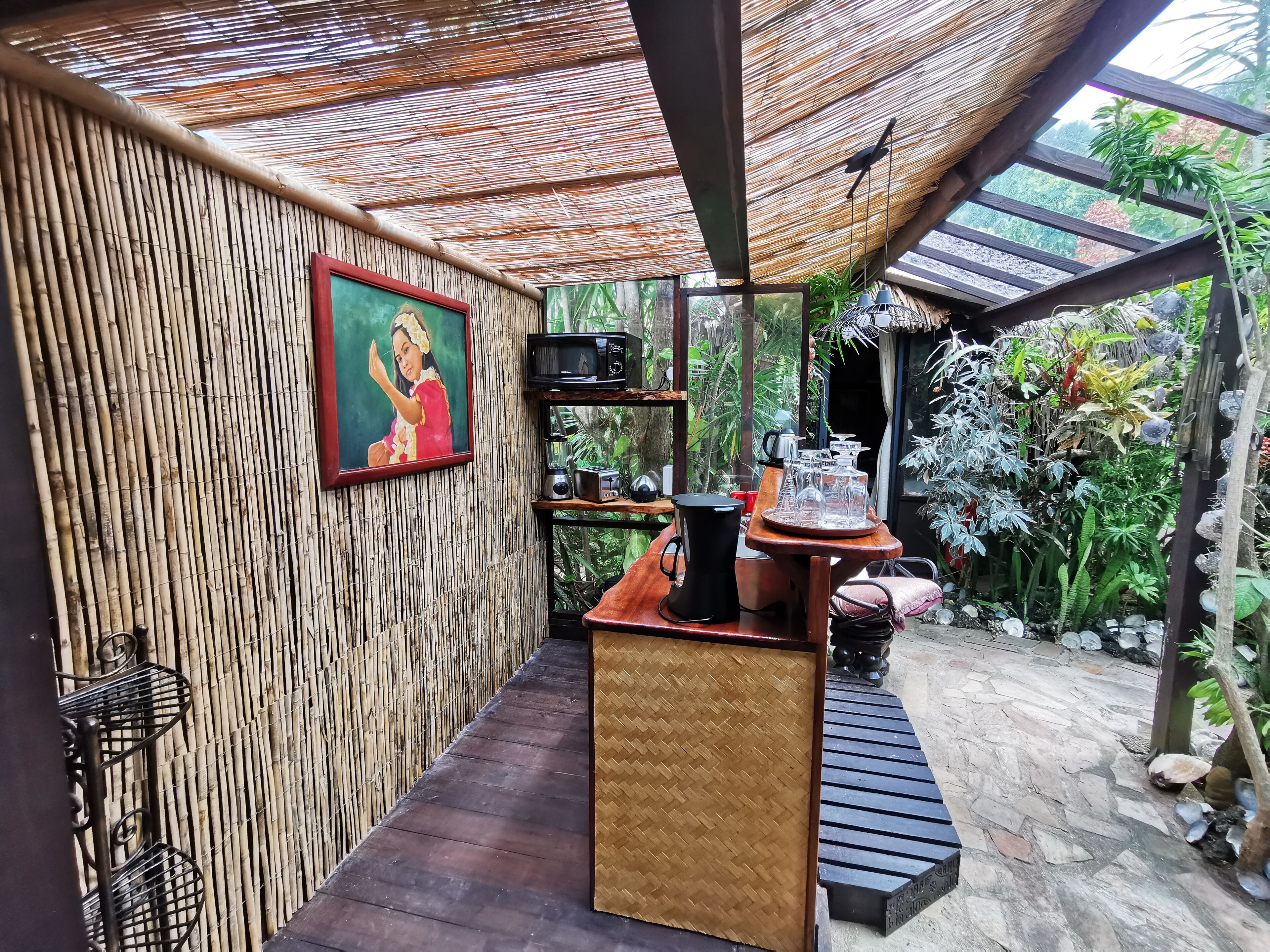 A bamboo-walled room with a wooden bench, a black coffee pot, and a shelf with kitchen items.