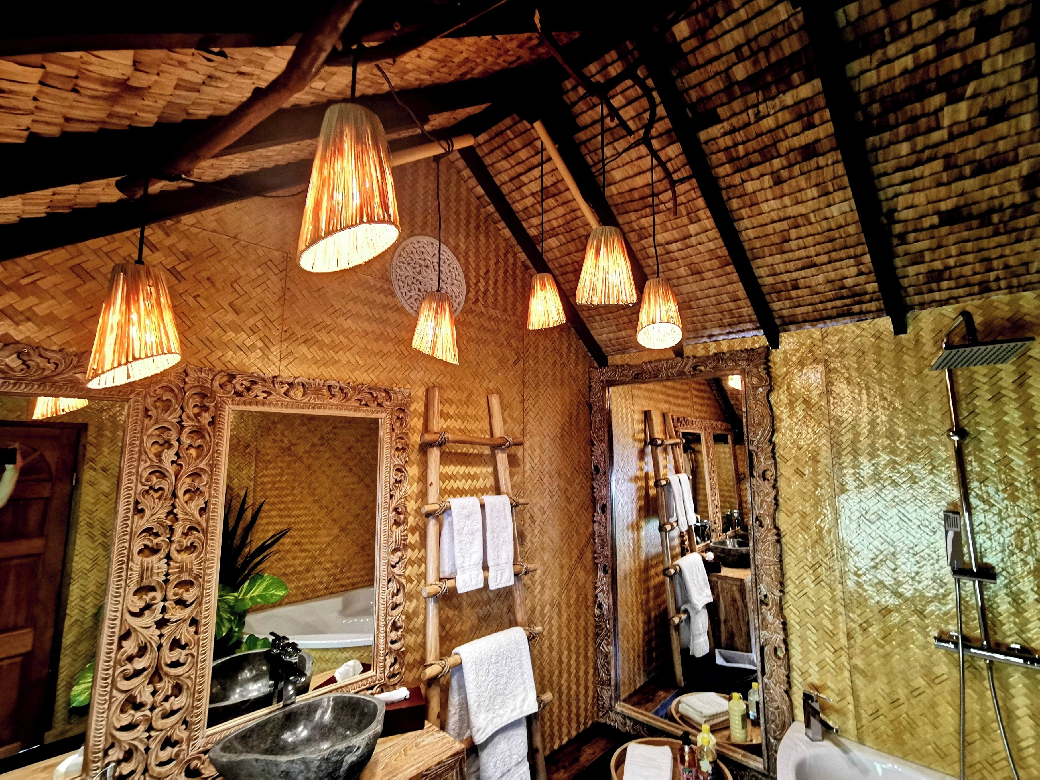 A rustic bathroom with a large mirror, hanging lights, and a wooden ceiling.