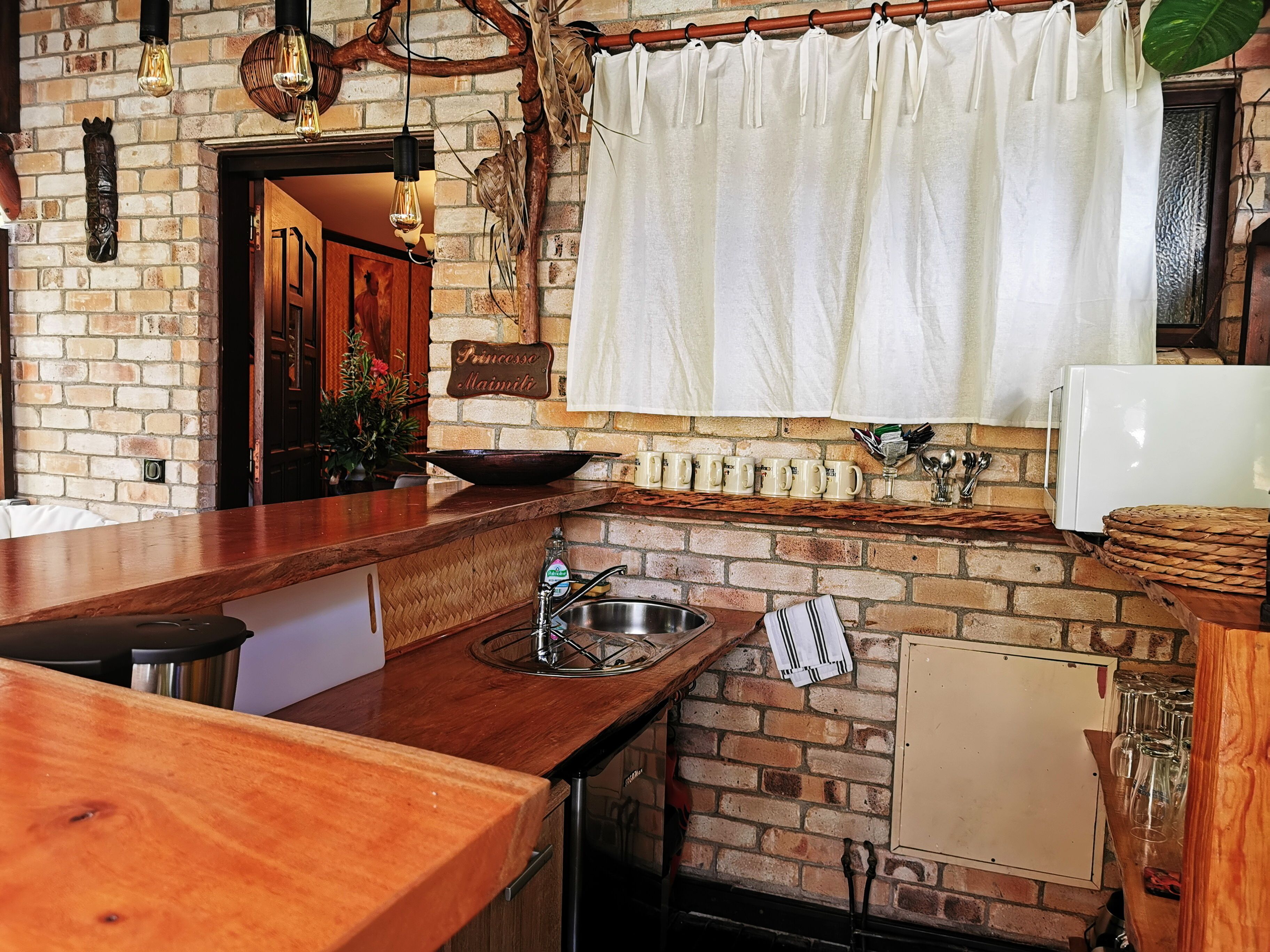 A kitchen with a brick wall, wooden countertop, and a white sink.