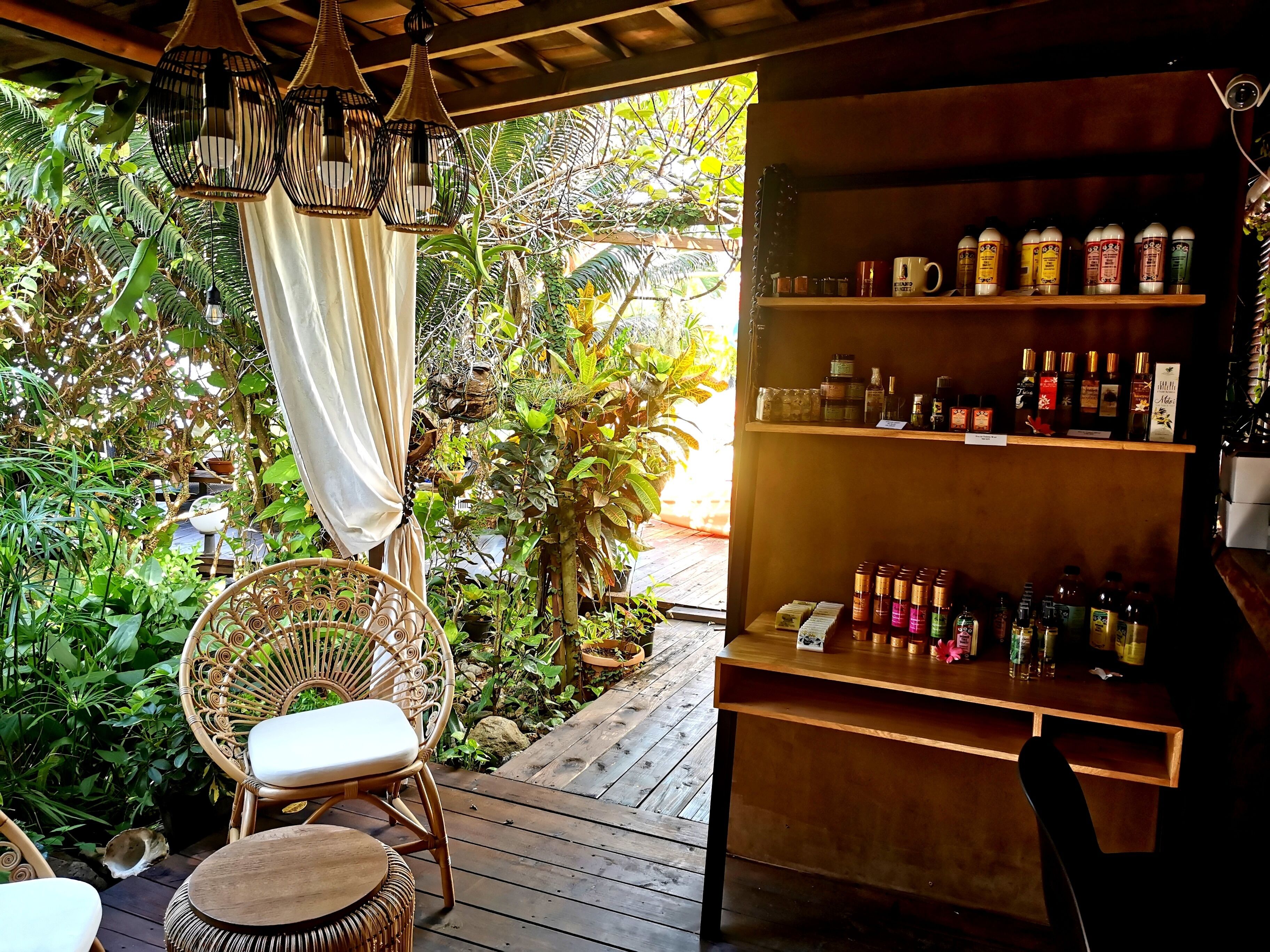 A wooden deck with wicker furniture, surrounded by lush greenery and a variety of bottles on shelves.