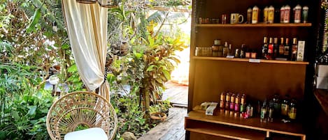 A wooden deck with wicker furniture, surrounded by lush greenery and a variety of bottles on shelves.