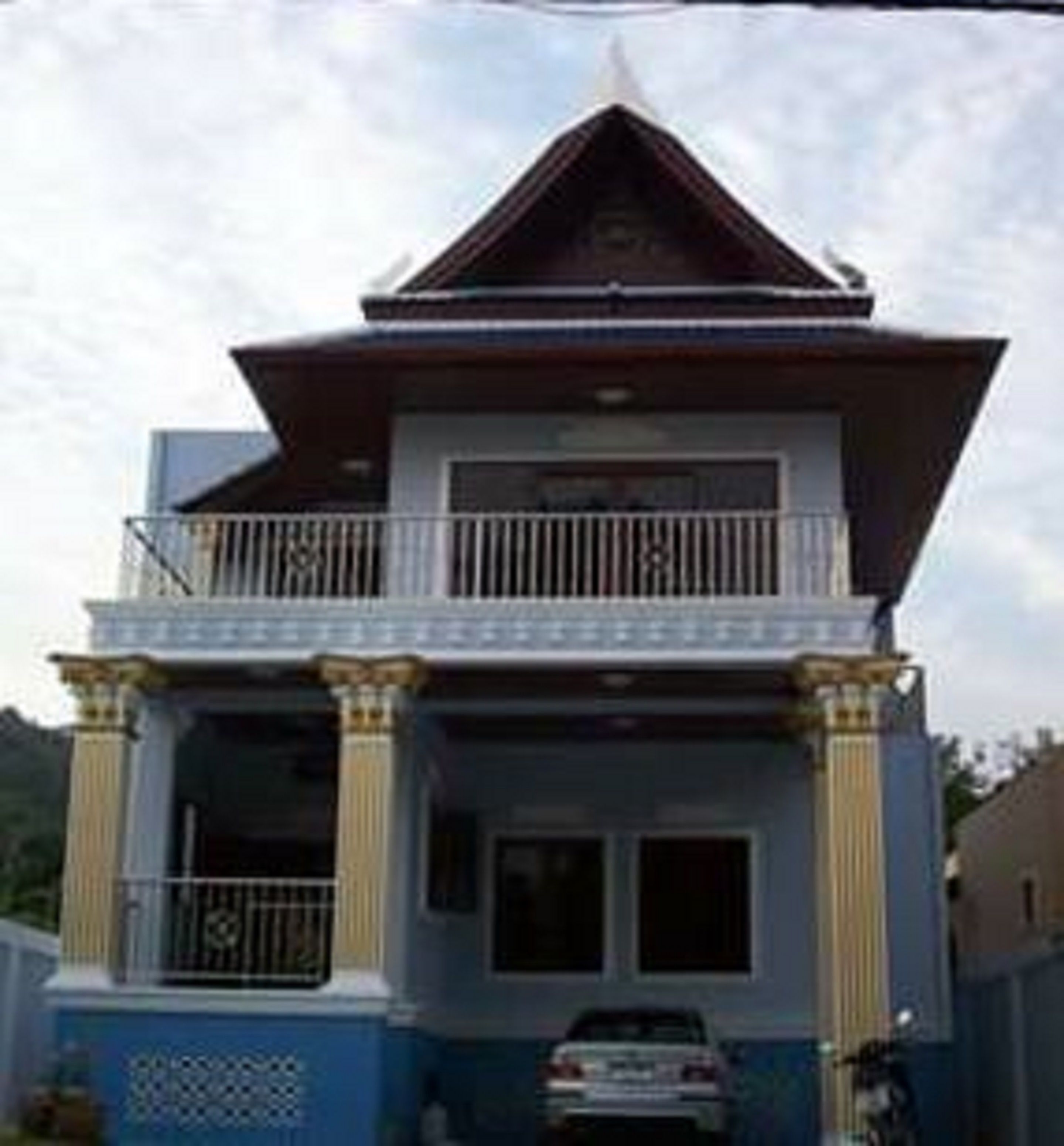 A two-story house with a balcony, columns, and a car parked in front.