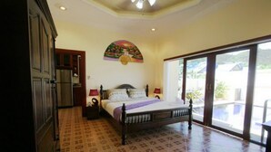 A bedroom with a bed, a nightstand, a wall-mounted lamp, and a large window with a view of the outside.
