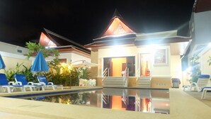 A pool area with lounge chairs and a building with a staircase leading to an entrance.