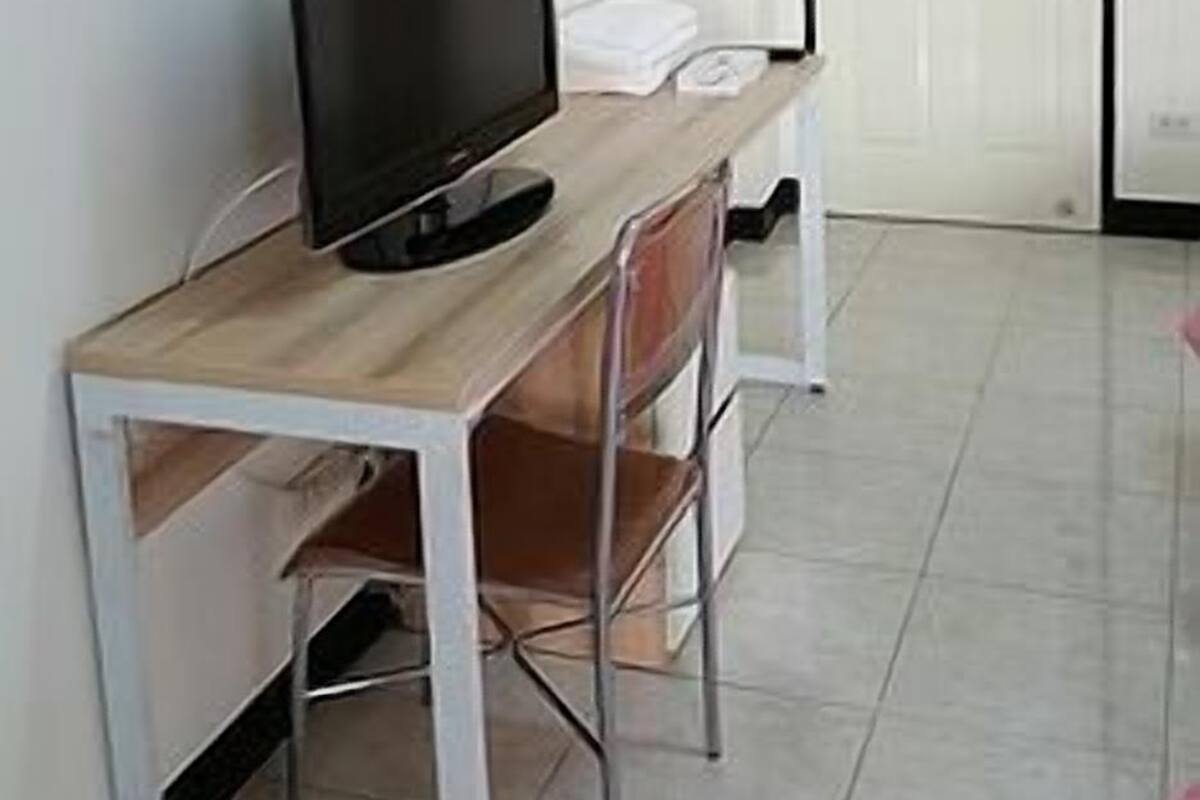 Una habitación con un escritorio de madera, televisor, una silla, una puerta blanca y piso de baldosas.