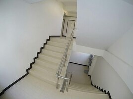 Una escalera con barandilla, paredes blancas y una puerta al final.