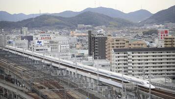 A train station with multiple tracks and a train on the right. There are buildings and mountains in the background.