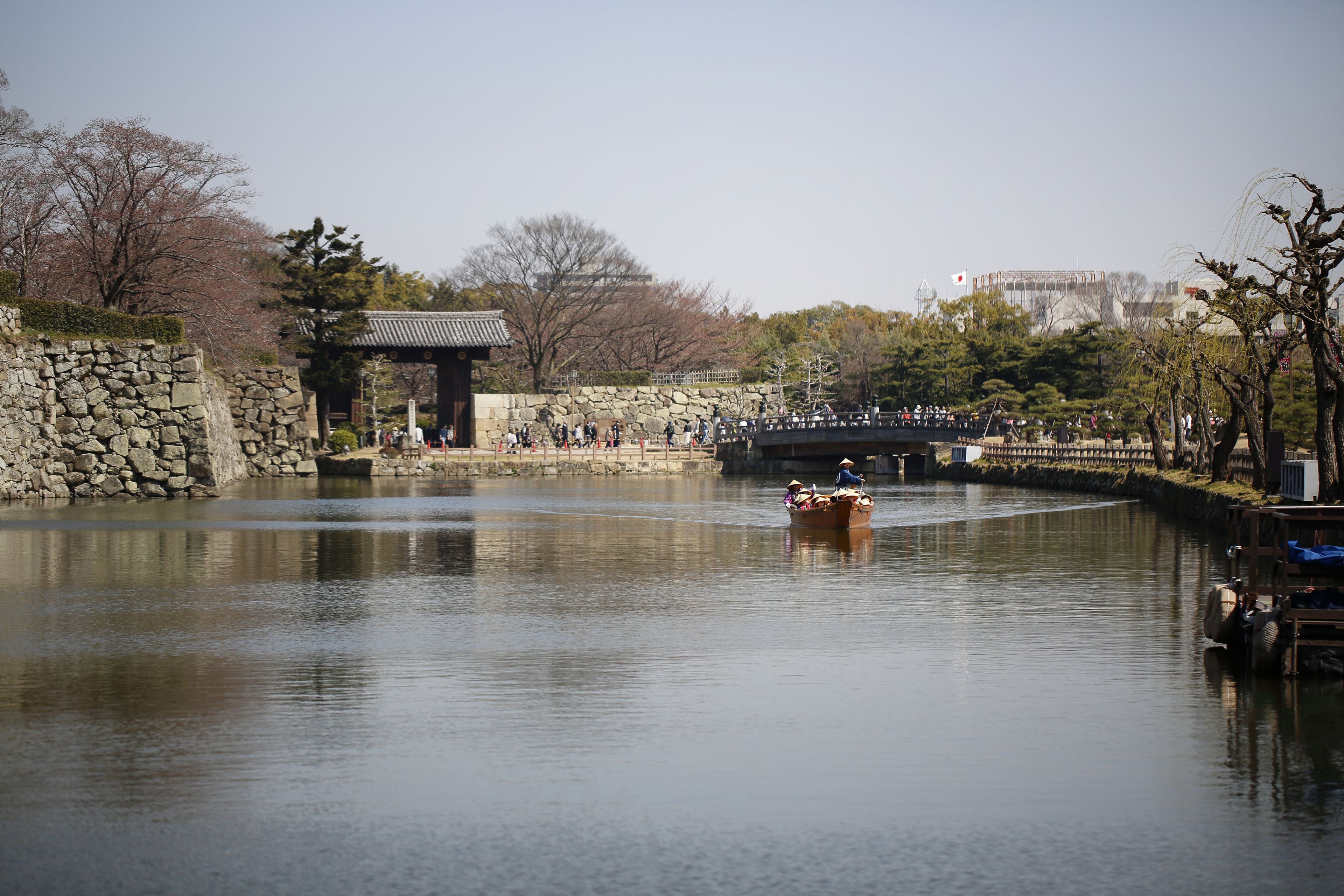 A calm river with a traditional boat, stone walls, and a pavilion.