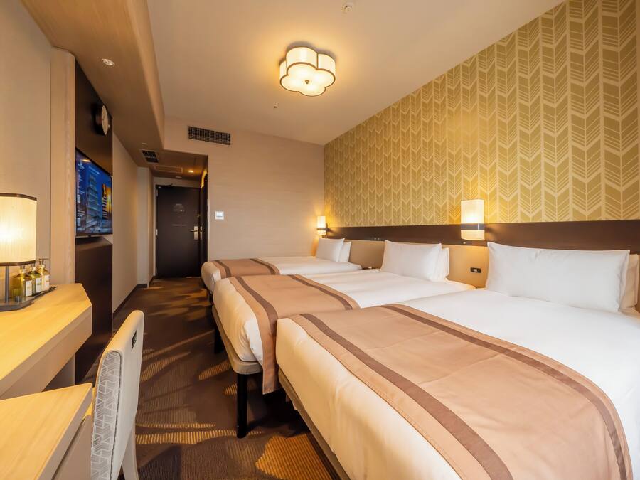 A hotel room with two beds, a desk with a lamp, a TV, and a patterned wall.