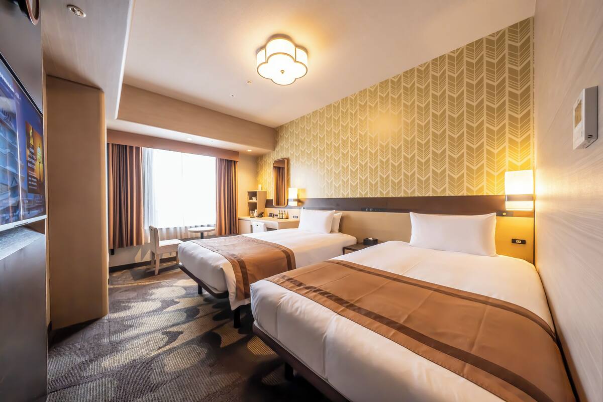 Hotellihuone, jossa on kaksi sänkyä, työpöytä, tuoli ja televisio.