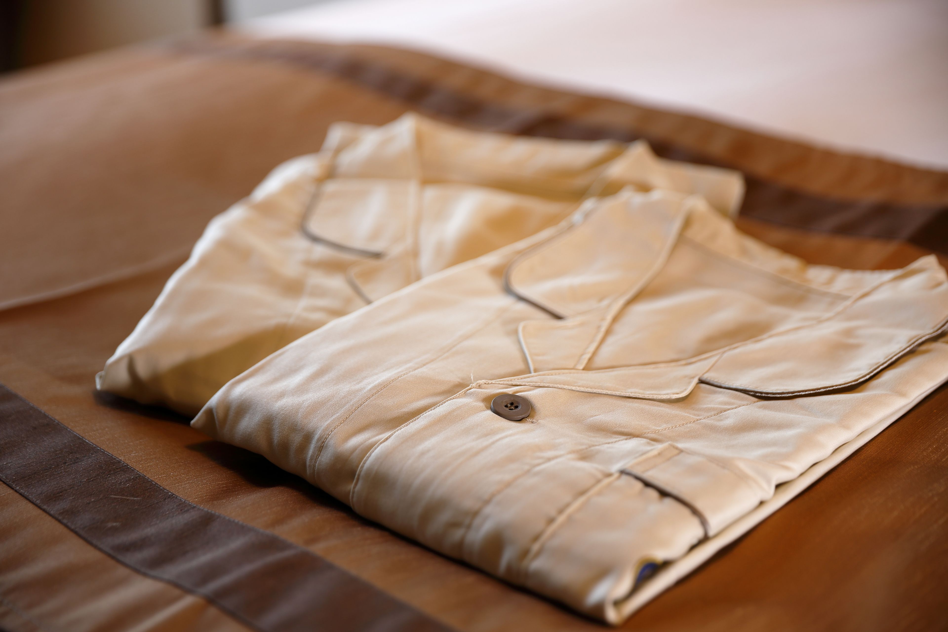 Neatly folded beige shirts on a brown bedspread.