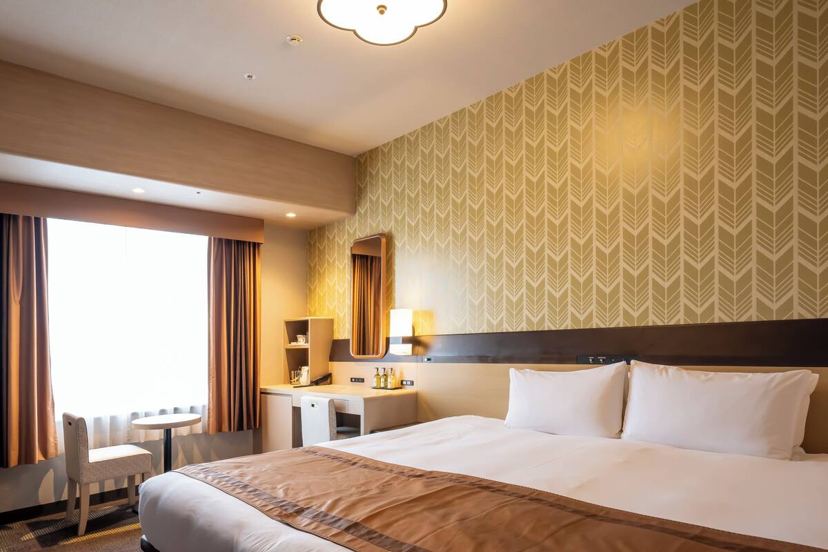 Hotellihuone, jossa on suuri sänky, työpöytä tuolilla, pieni pöytä ja peili.