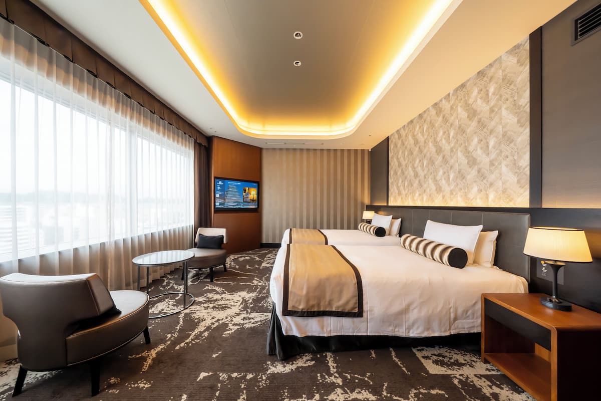 A hotel room with a large bed, two bedside tables, a desk, a chair, and a TV.