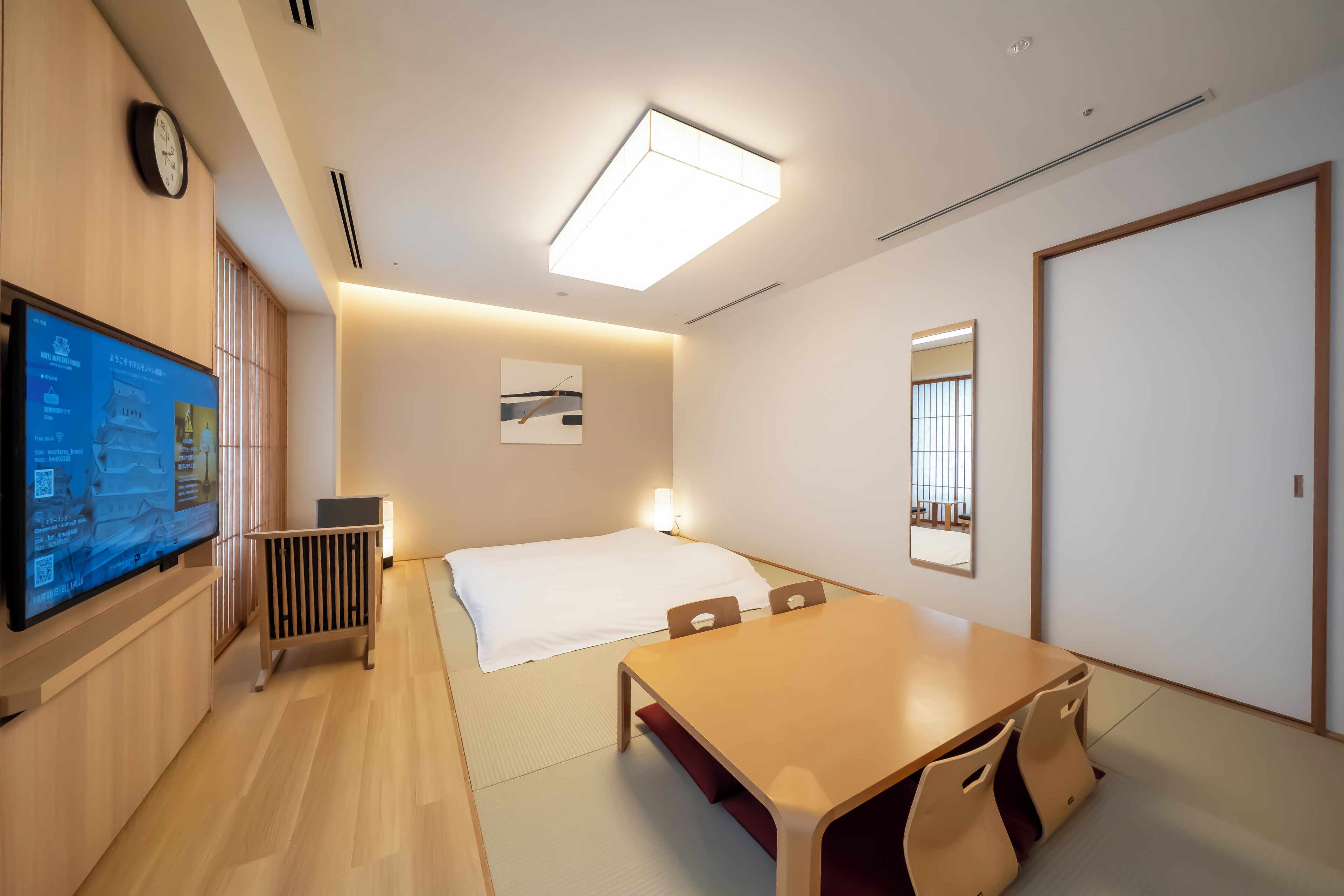 A modern hotel room with a bed, a desk, a television, and a large window.