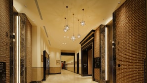 Un vestíbulo de hotel con suelo de mármol, paredes de ladrillo y candelabros modernos.