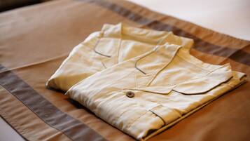A neatly folded beige shirt on a bed with a brown and beige striped bedspread.