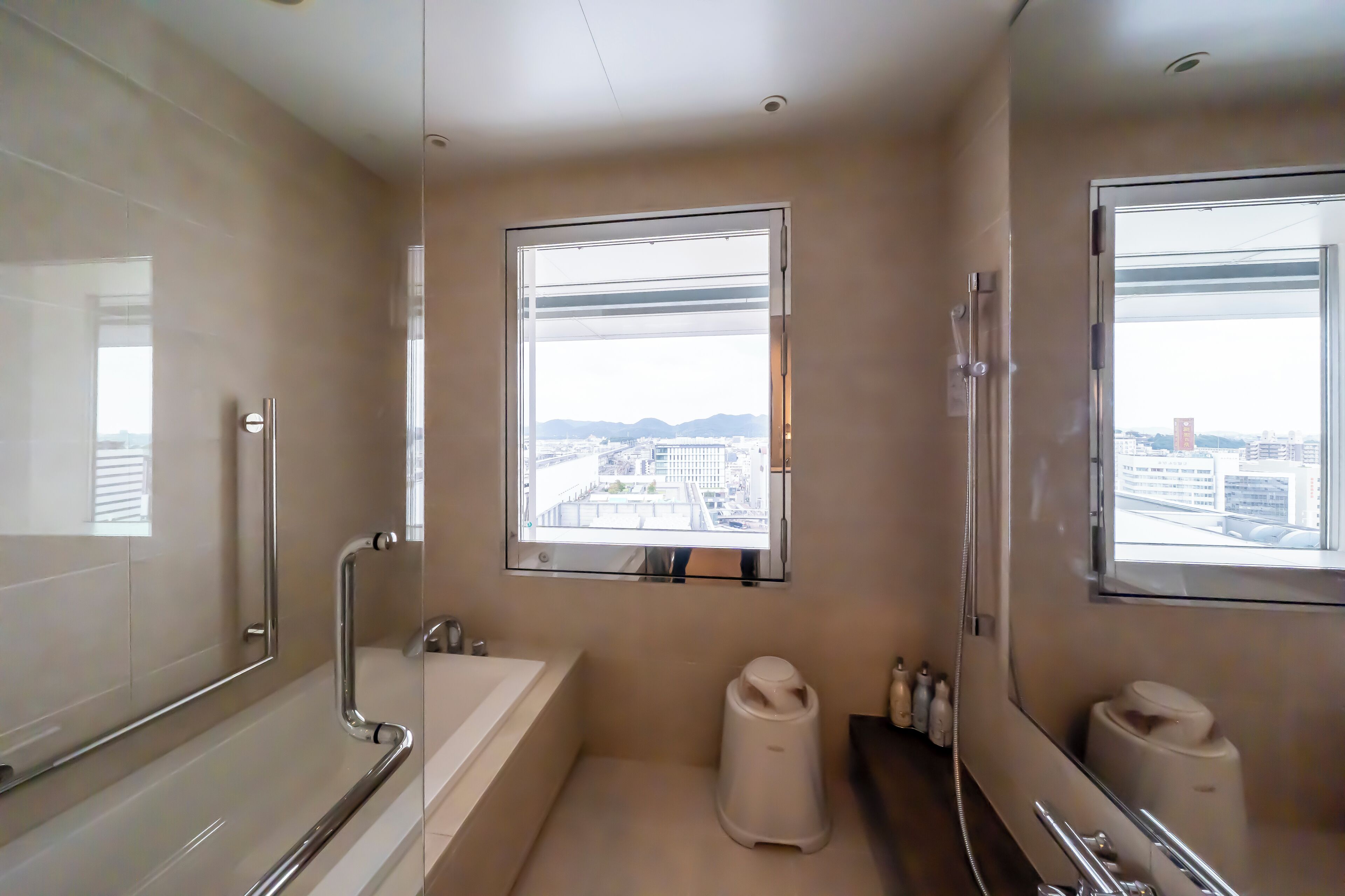 A modern bathroom with a bathtub, toilet, and sink, featuring large windows with a city view.