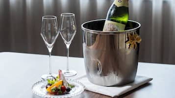 A champagne bottle in a metallic bucket with two empty glasses and a fruit platter on a table.