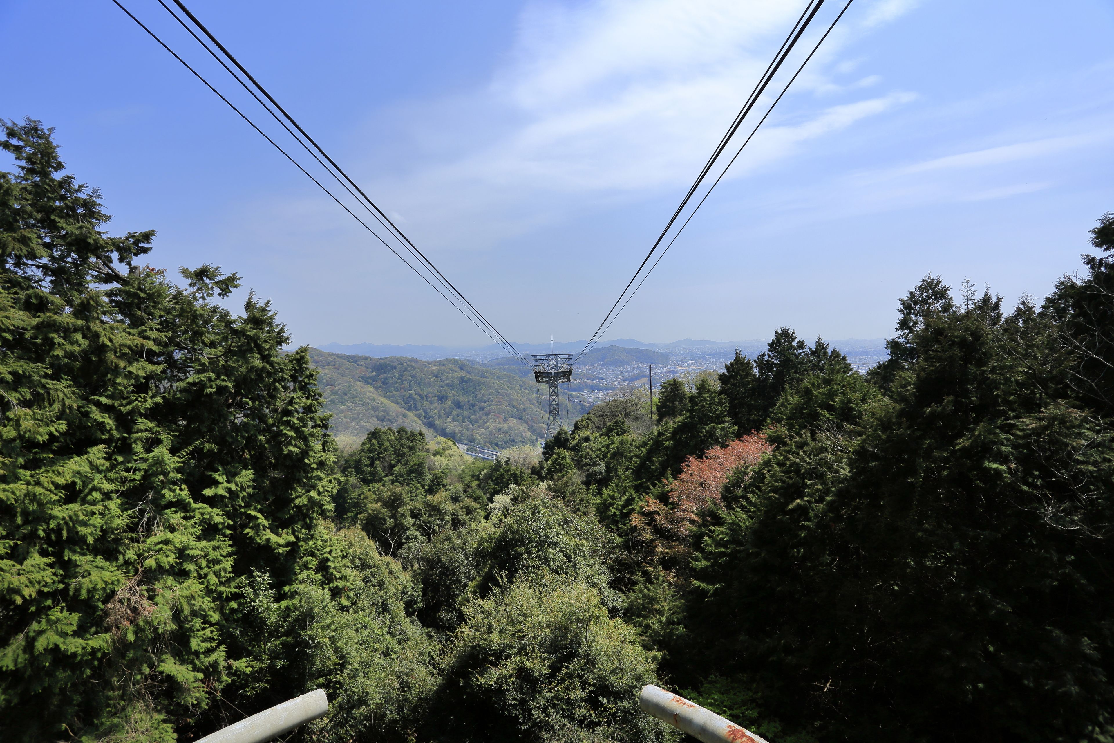 Eine Seilbahnanlage inmitten dicht bewaldeter Hügel, mit blauem Himmel und fernen Bergen.
