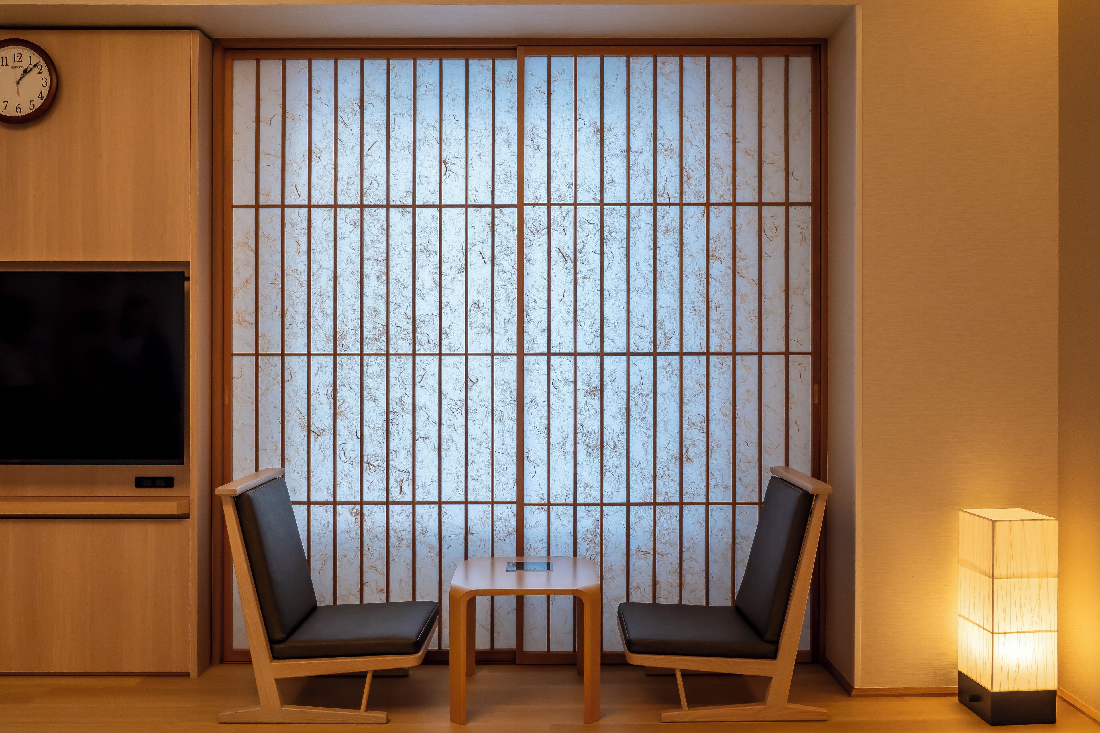 A room with a large shoji screen, two chairs, a small table, a TV, and a floor lamp.