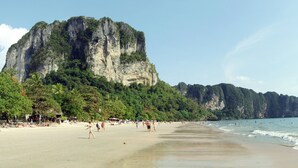 Une plage avec une grande falaise, des palmiers et des gens sur le sable.