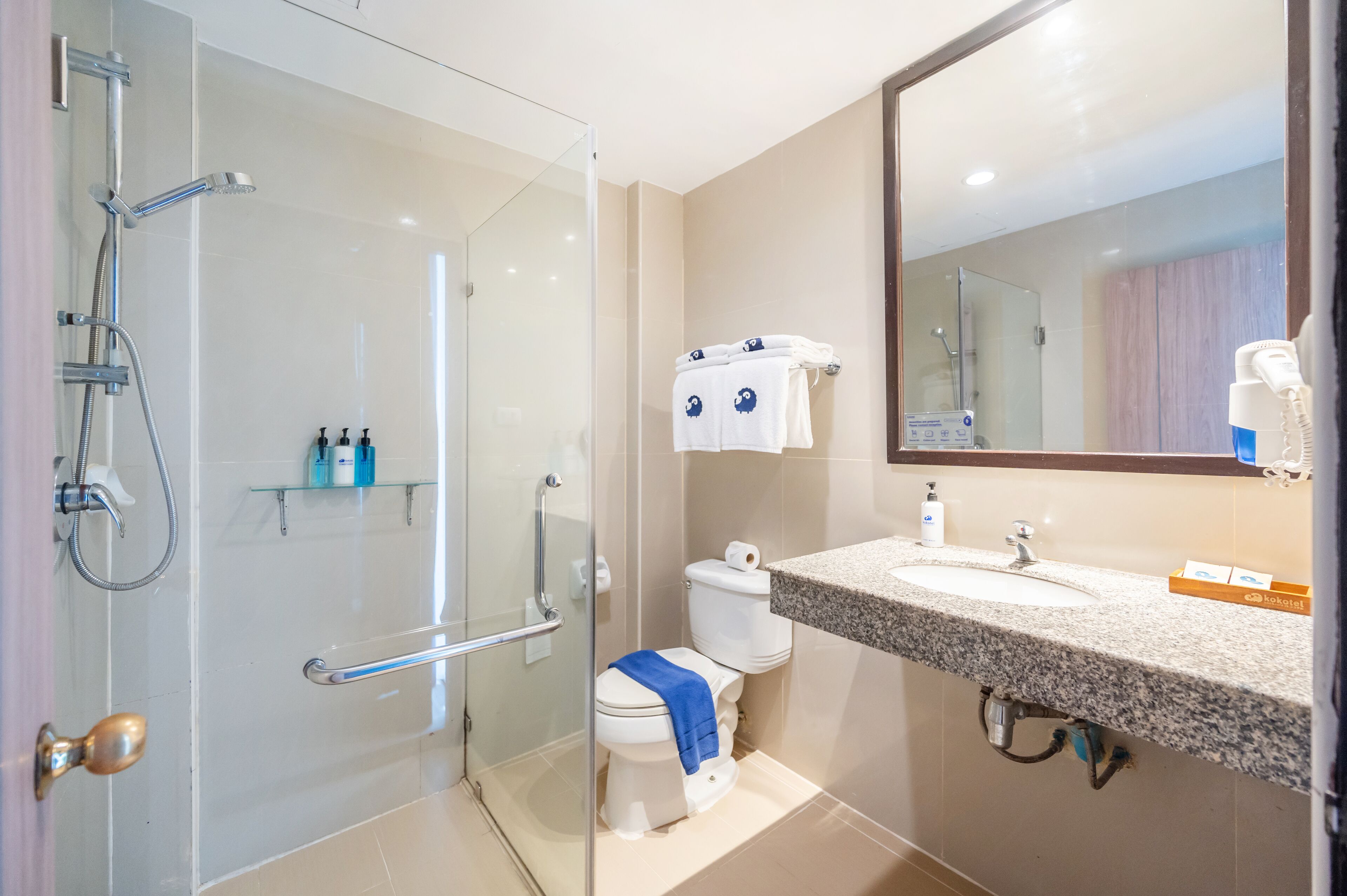 A modern bathroom with a glass shower enclosure, a toilet with a blue towel, and a sink with a mirror above it.