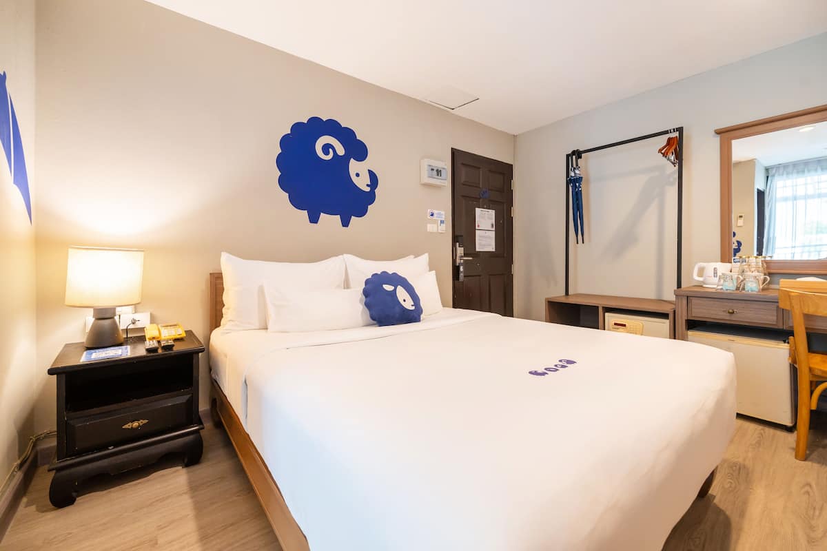 Una habitación de hotel con cama, mesita de noche con lámpara, cómoda y espejo.