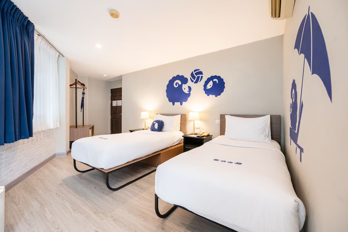 Habitación de hotel con dos camas, un armario, un espejo y una pared decorada con siluetas de ovejas y paraguas.
