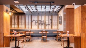 Un restaurant avec des tables et des chaises en bois, un mur de briques orné d’un slogan et une verrière au-dessus de l’espace réservé aux clients.