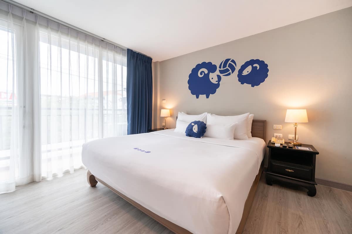 Habitación de hotel con una cama grande, dos lámparas de noche, una mesita de noche y un ventanal con cortinas.