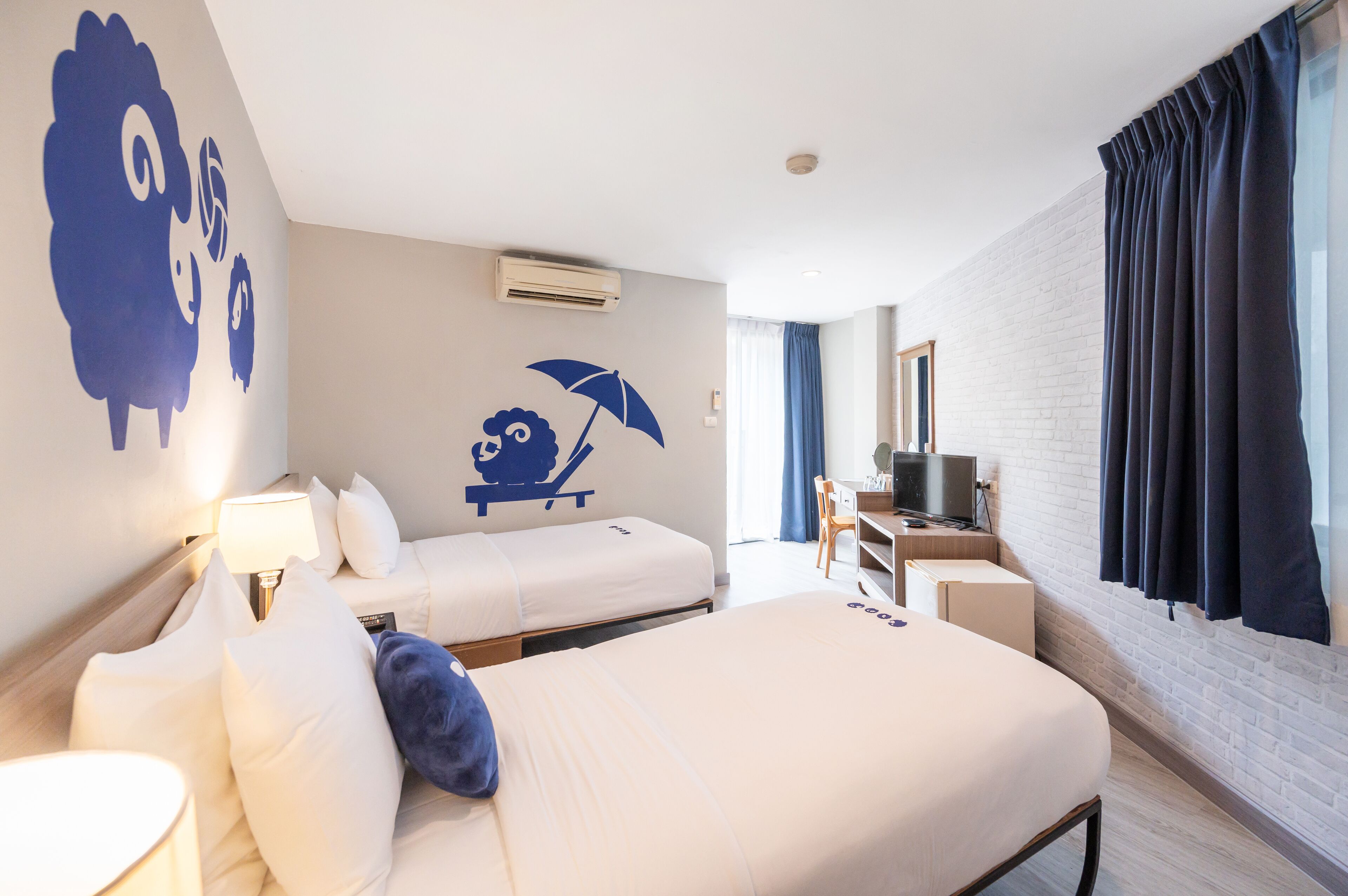 A hotel room with two beds, a desk, a TV, and a large window with curtains.
