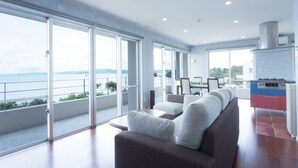 A modern living room with a sofa, a coffee table, and a view of the sea through large windows. - Suite villa Yagaji (Nago)
