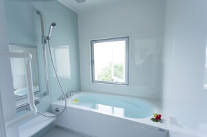 A modern bathroom with a large bathtub, a showerhead, and a window providing natural light.