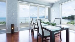 A dining area with a table and chairs, large windows with a view of the sea, and a balcony with plants. - Suite villa Yagaji (Nago)