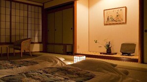 Una habitación japonesa tradicional con suelo de tatami, una mesa baja con un florero y un cuadro en la pared.