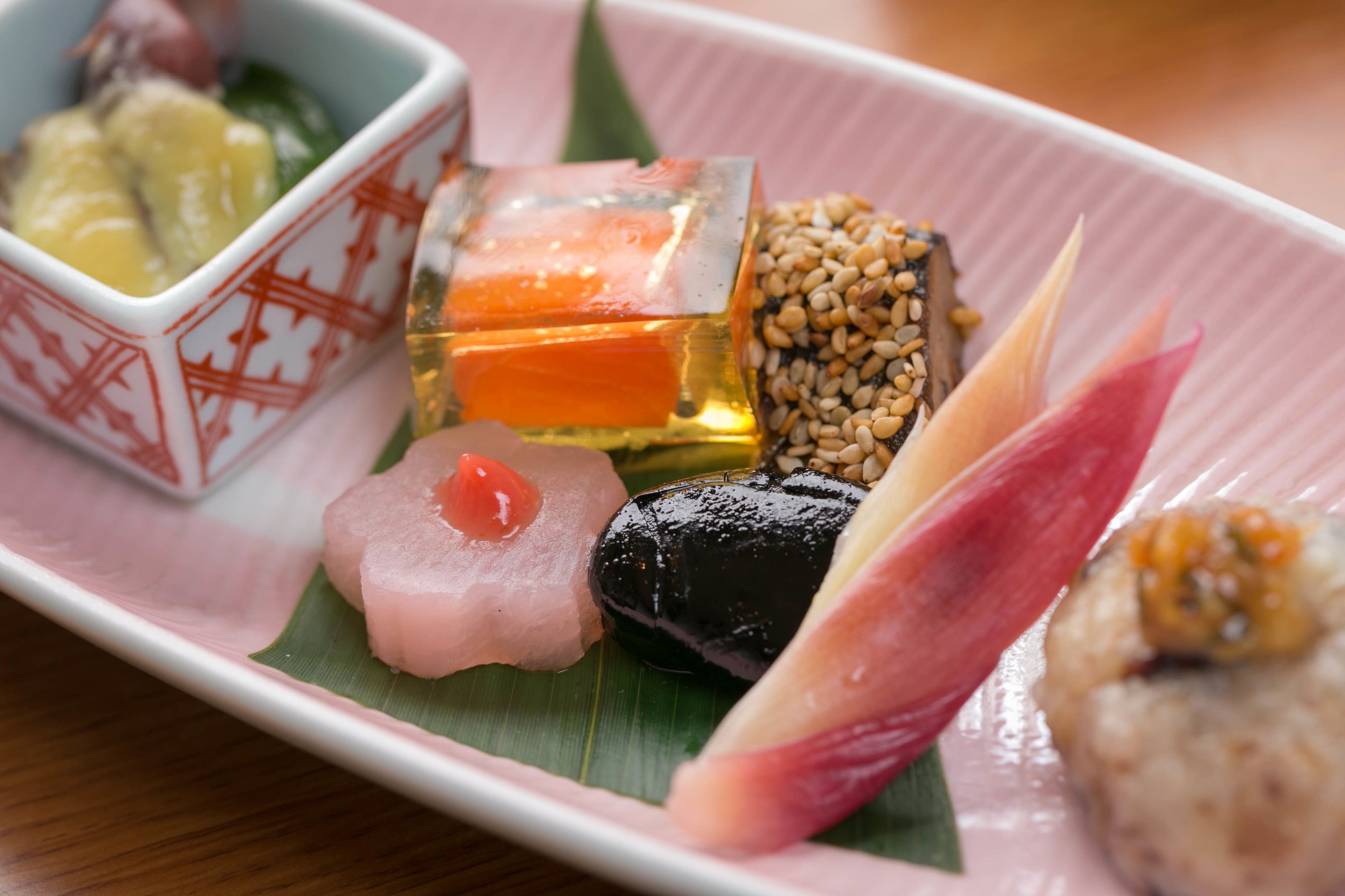 A variety of sushi dishes on a pink plate with a green leaf.