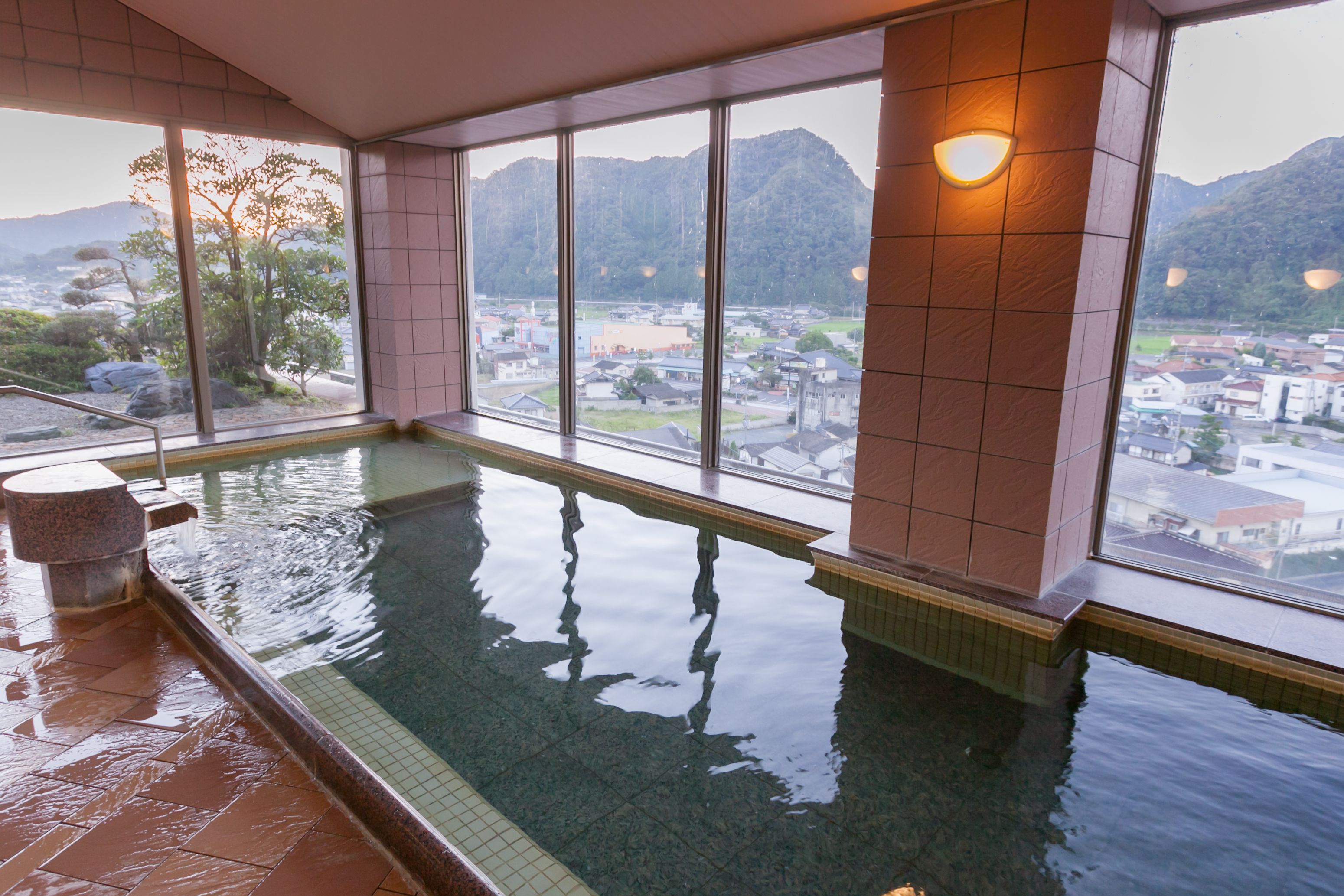 Una piscina interior con vistas a un pueblo y montañas a través de amplios ventanales.
