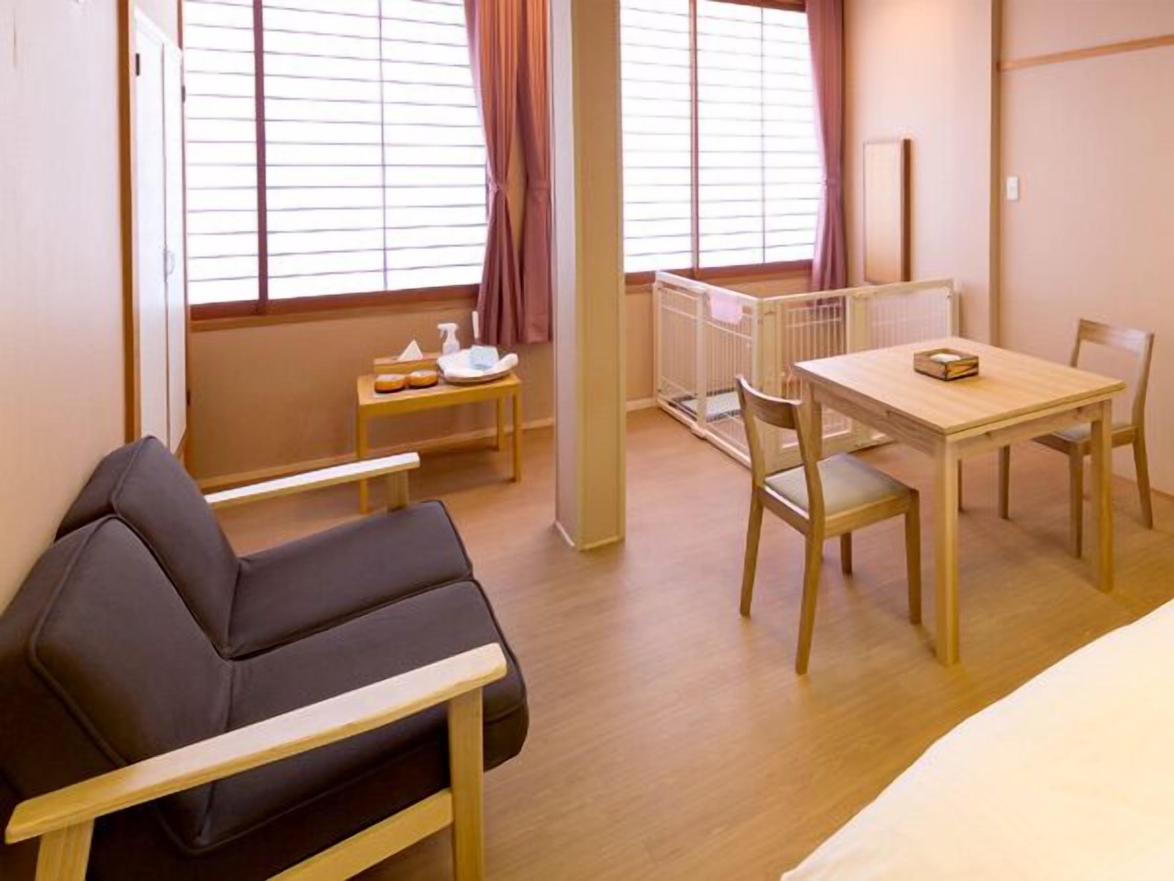 Una habitación con una cama, una pequeña mesa con una silla, un banco y una ventana con cortinas.
