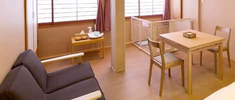 Una habitación con una cama, una pequeña mesa con una silla, un banco y una ventana con cortinas.