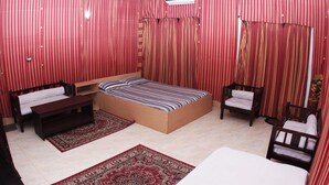 Een slaapkamer met een enkel bed, een houten bankje, twee stoelen en een groot rood vloerkleed.