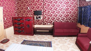Een kamer met behang met patroon, een rode bank, een houten kast en een televisie op een standaard.