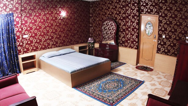 Een slaapkamer met een bed, een dressoir, een spiegel, een deur en een rode stoel.