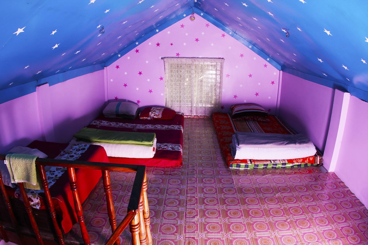 A room with two beds, a window with lace curtains, and a patterned floor.