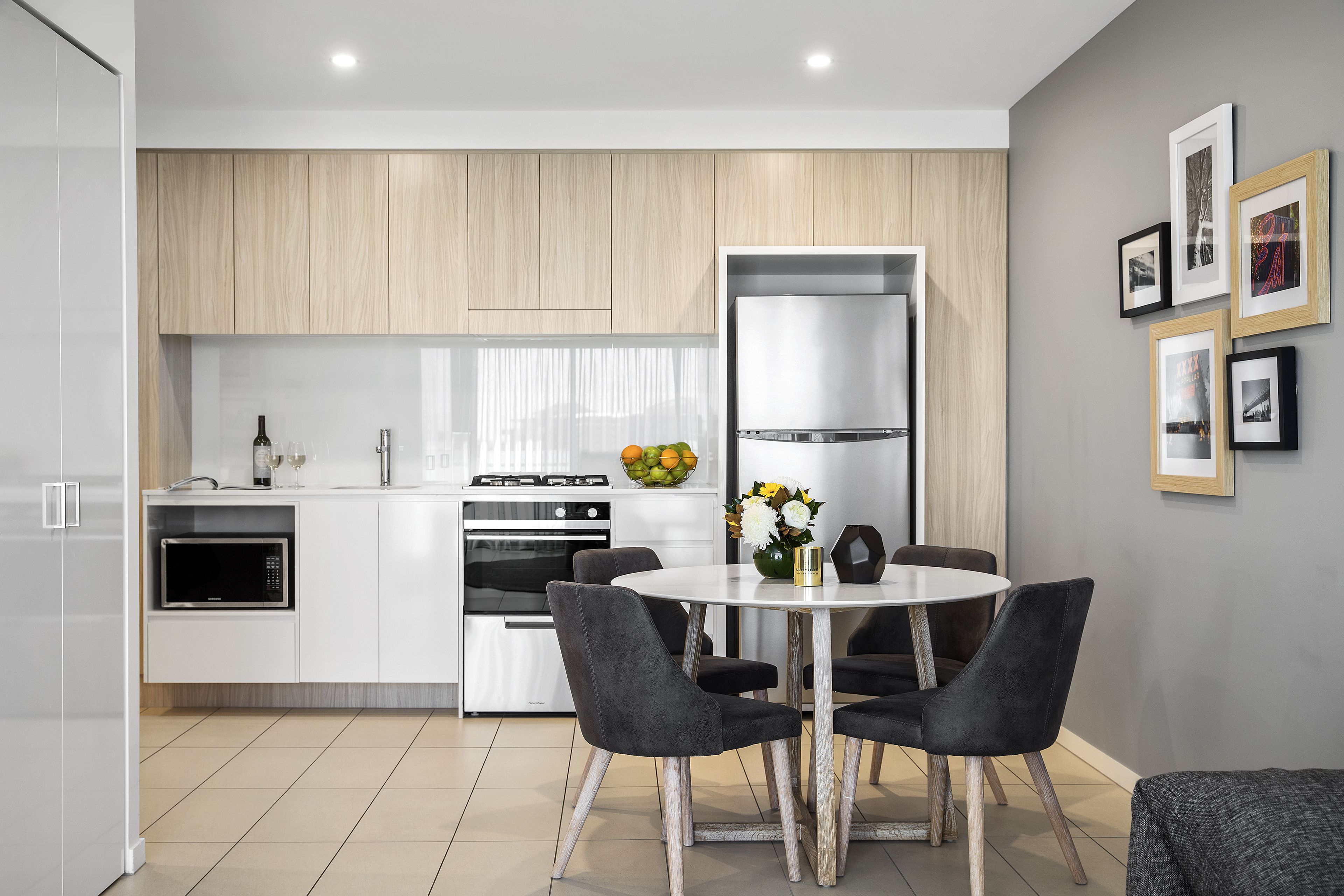 A modern kitchen with white cabinetry, a built-in oven, and a dining area with a round table and four chairs.