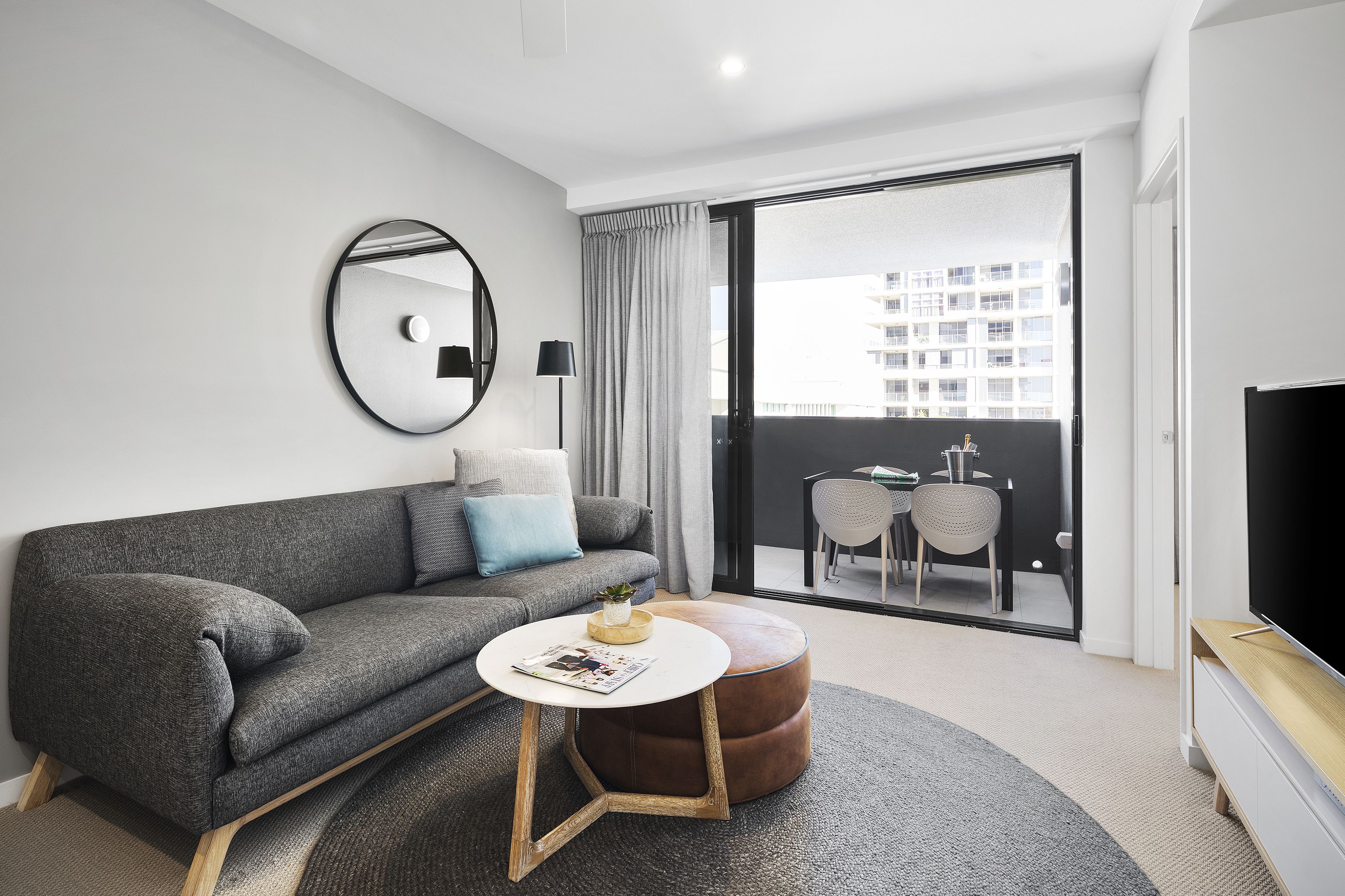 Un salon moderne avec un canapé gris, une table basse ronde et un téléviseur à écran plat.