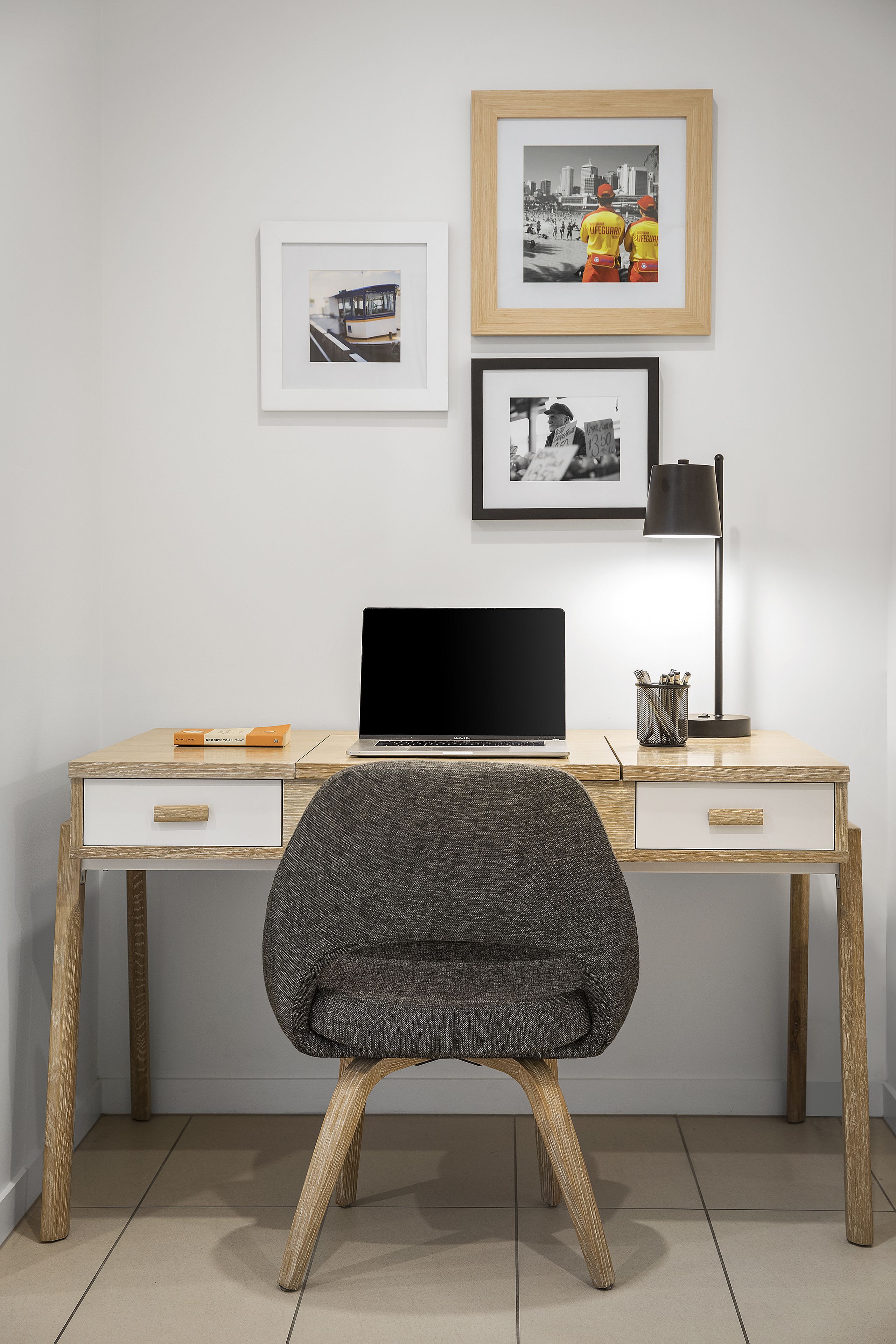 A modern workspace with a wooden desk, a laptop, and a chair. There are framed pictures on the wall.