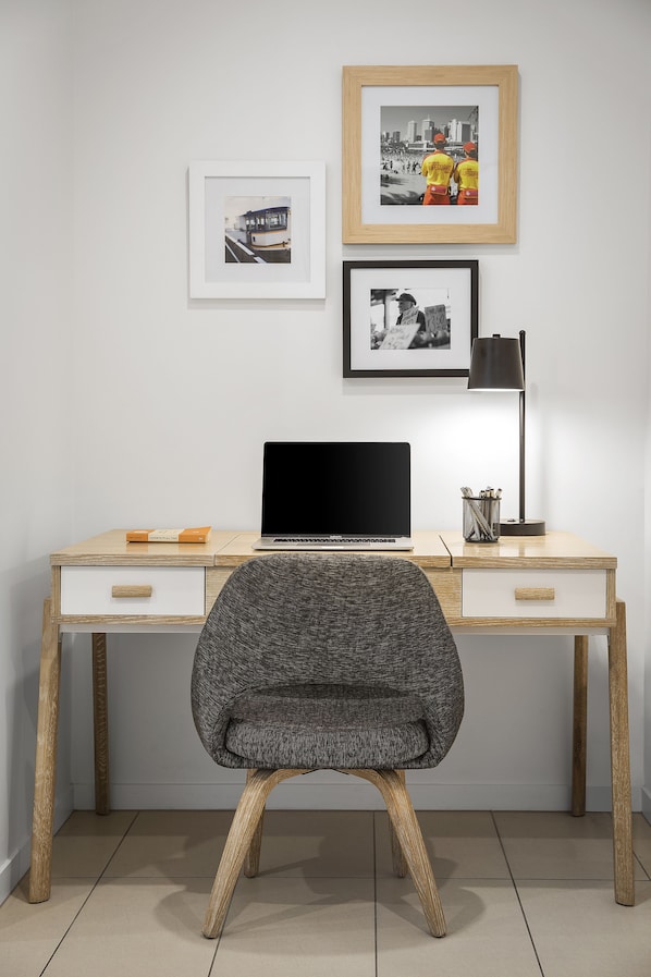 Un espacio de trabajo moderno con un escritorio de madera, una computadora portátil y una silla. Hay cuadros en la pared.