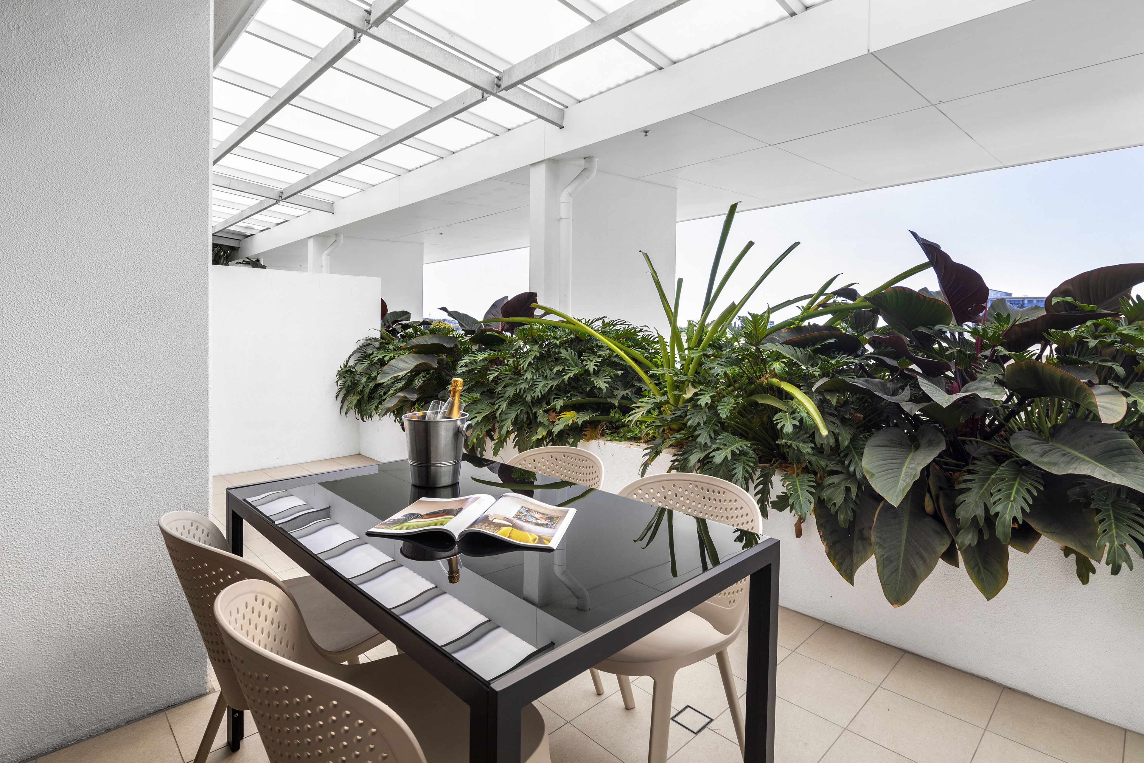 Een moderne eethoek buiten, met een glazen tafel, stoelen en weelderige beplanting.
