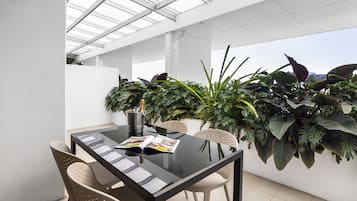 Een moderne eethoek buiten, met een glazen tafel, stoelen en weelderige beplanting.